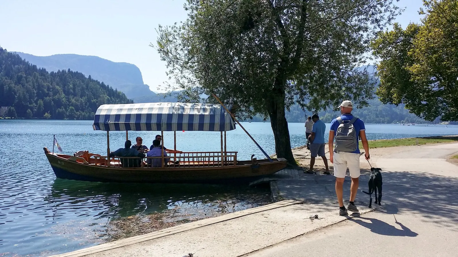 A moored pletna and Atena walking along the shore of Lake Bled